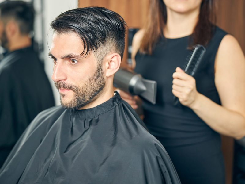Young assistant holding professional instruments in hands while going to dry wet hair