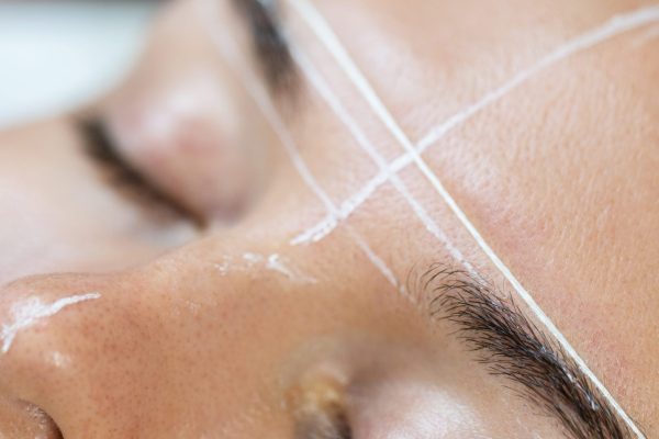 Young woman during professional eyebrow mapping procedure before permanent makeup